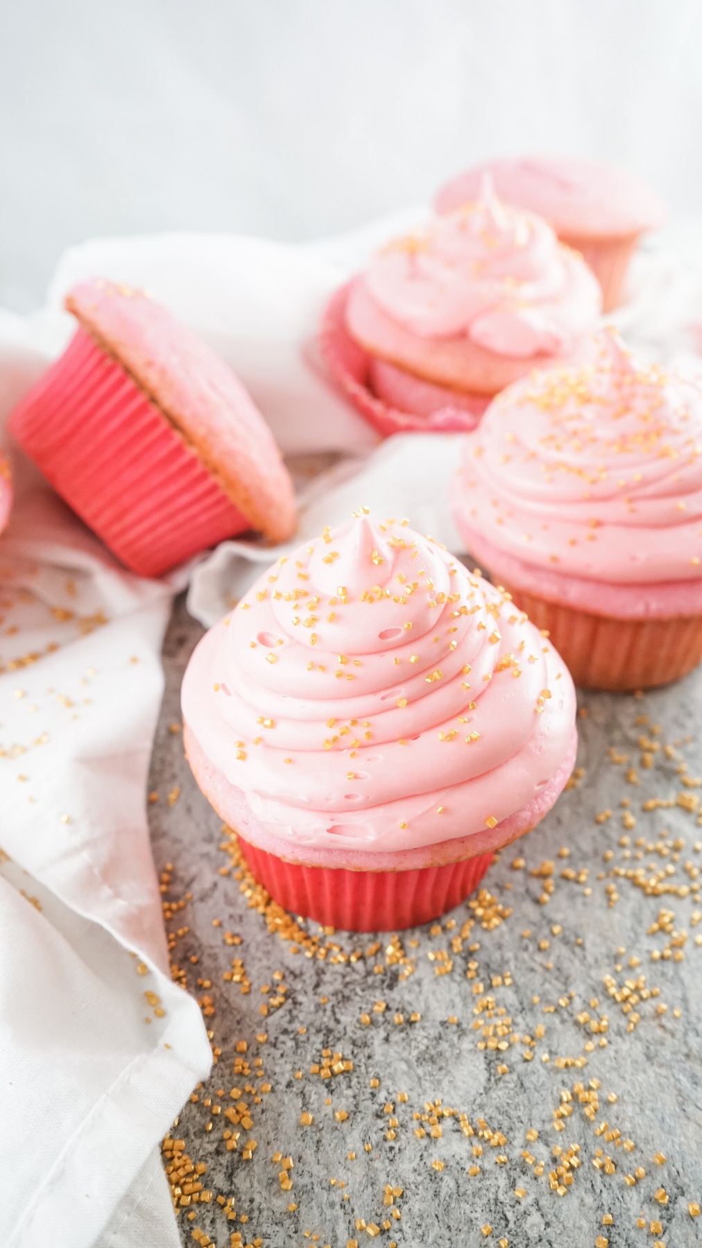 frosting the pink champagne cupcakes with gold sprinkles