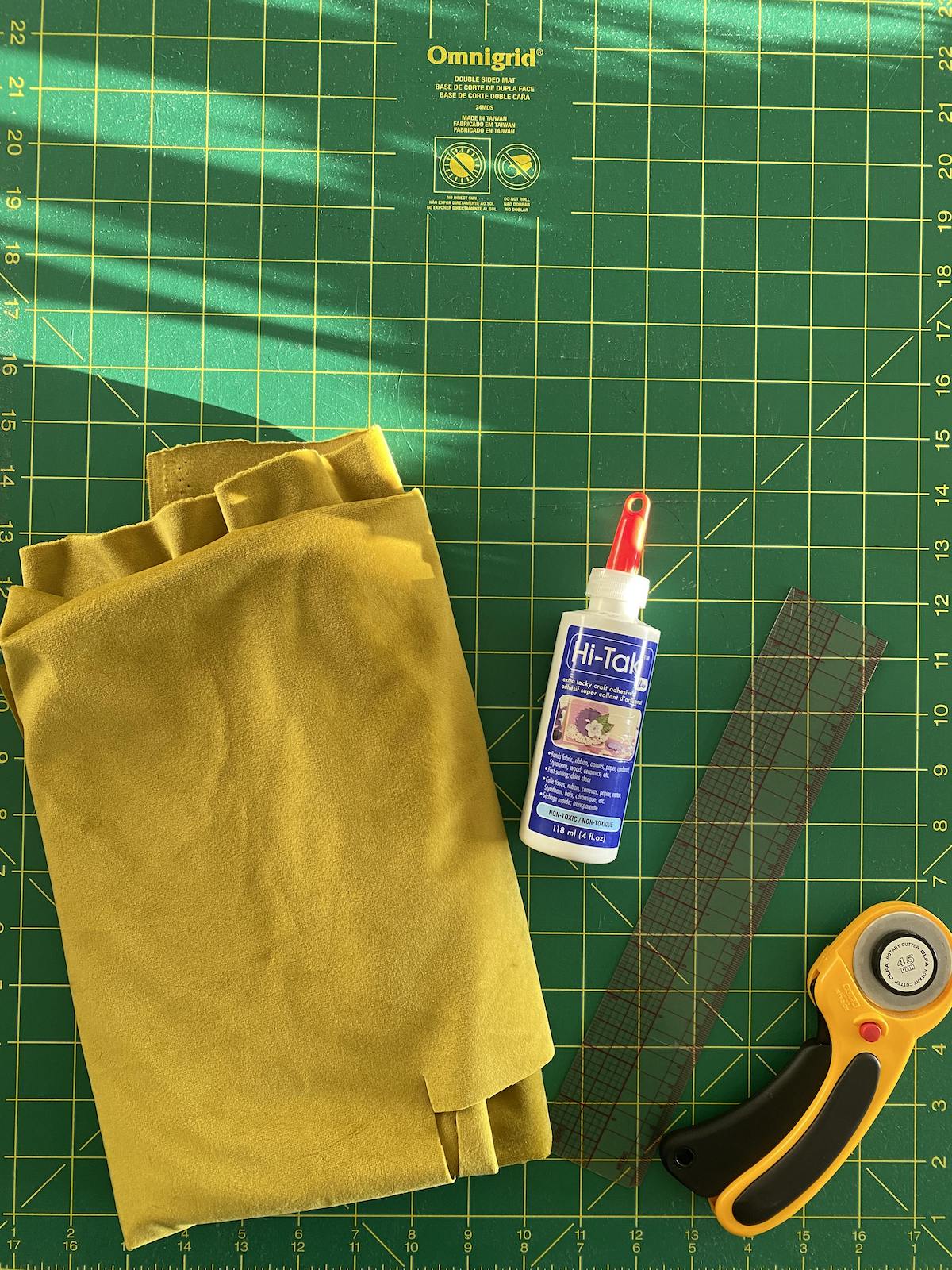 Velvet fabric, glue, a ruler and a rotary cutter sit atop a green cutting mat 